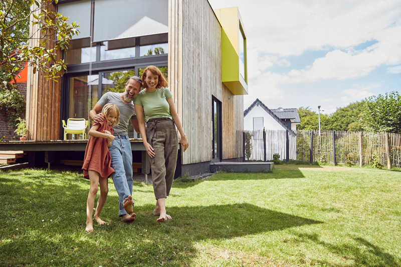 En familj på tre personer framför ett hus.